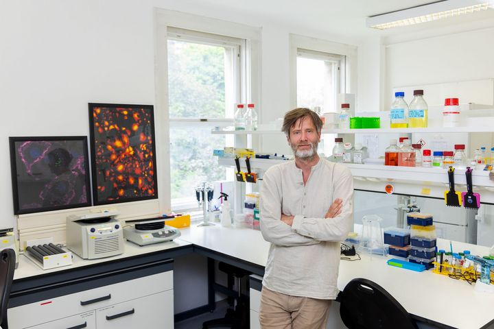Wissenschaftler mit verschränkten Armen in einem Labor mit Geräten und Bildern